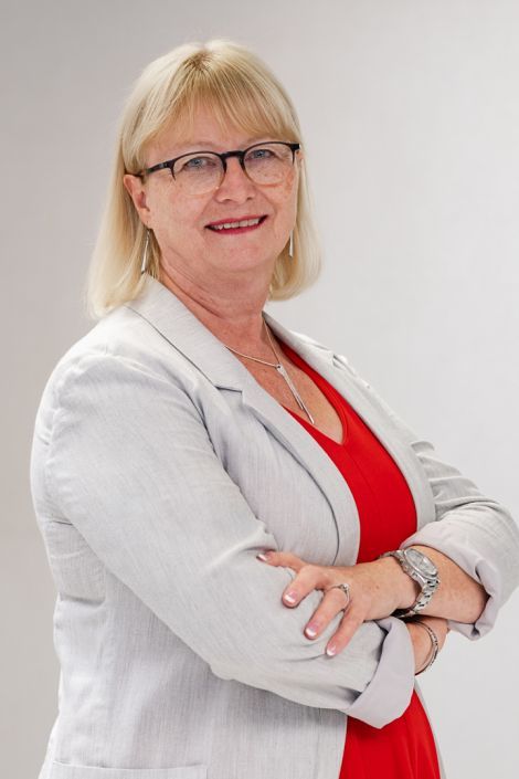 A woman wearing glasses and a red shirt is standing with her arms crossed