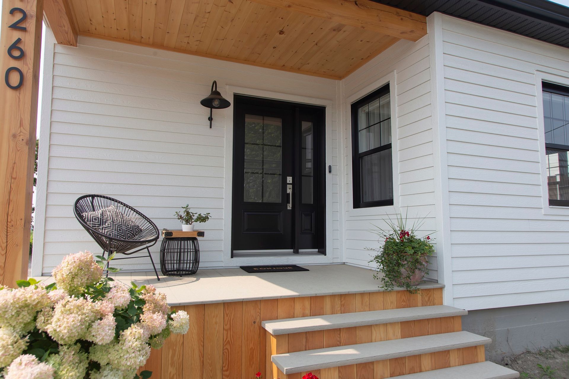 Une maison blanche avec une porte noire et une chaise sur le porche.