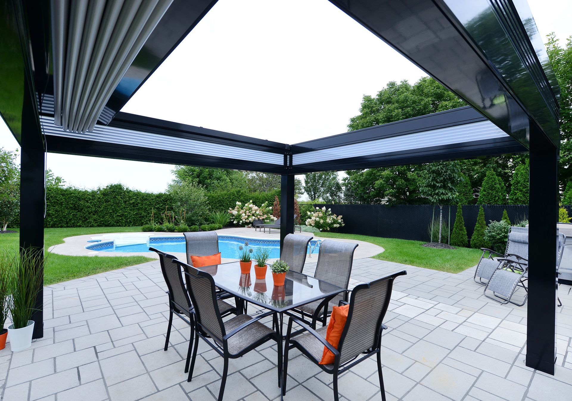 Un patio avec une table et des chaises sous une pergola à côté d'une piscine.