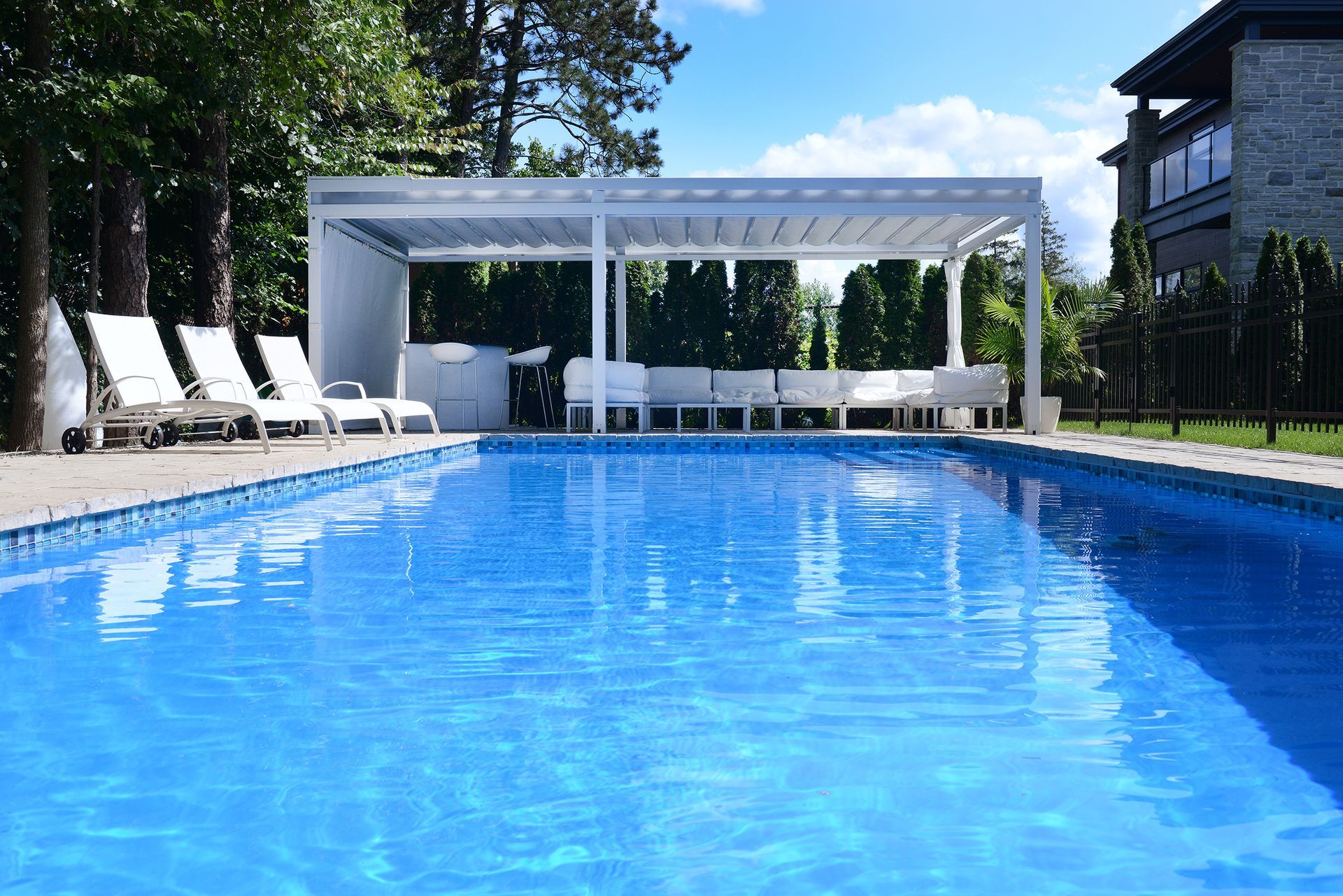 Une grande piscine avec une pergola blanche et des chaises autour.