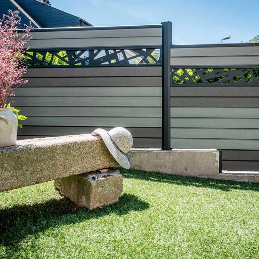Un chapeau repose sur un banc en pierre dans une cour arrière avec une clôture composite grise moderne et une pelouse verte.