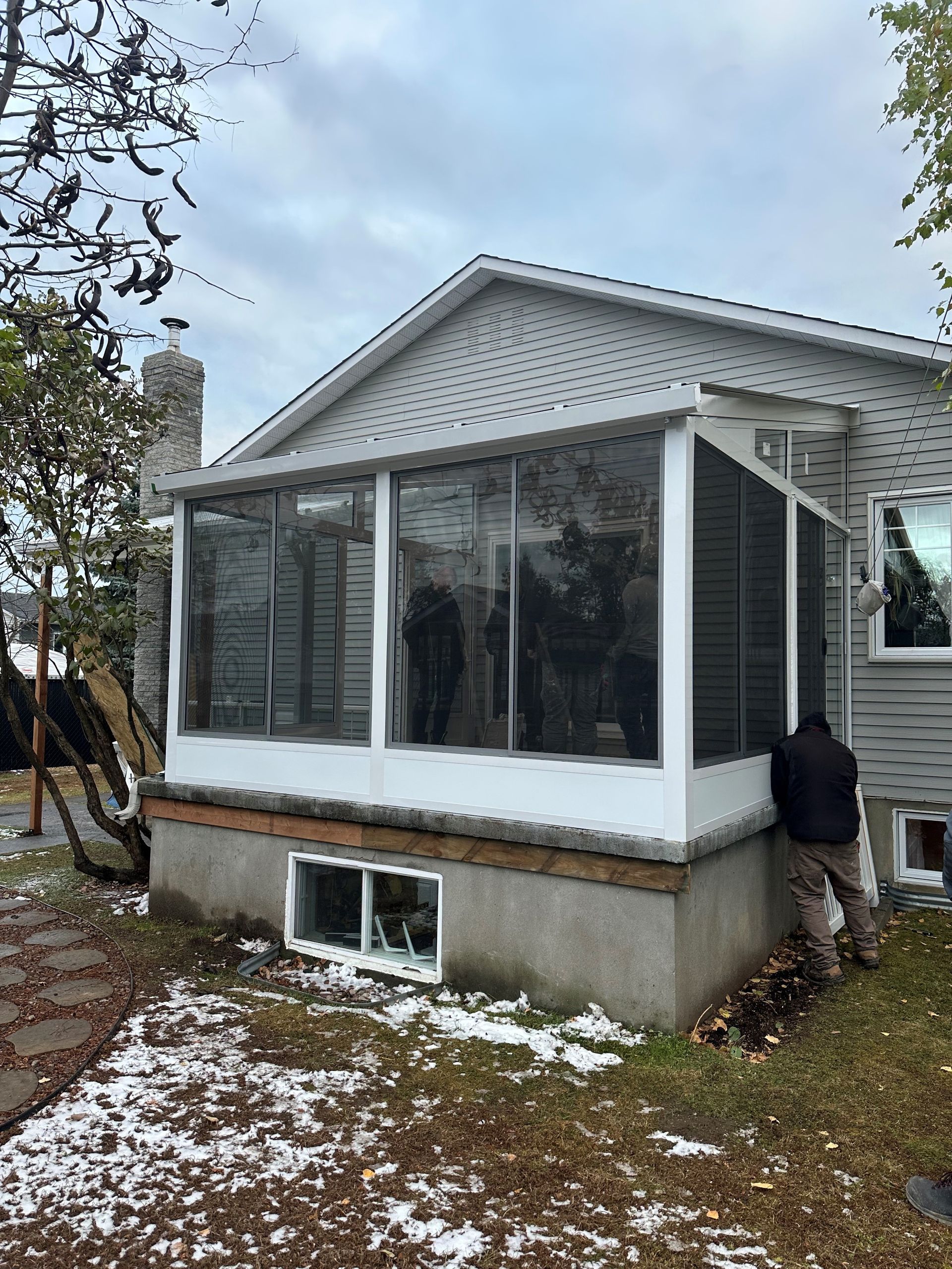 Un homme se tient devant une maison avec une véranda grillagée.