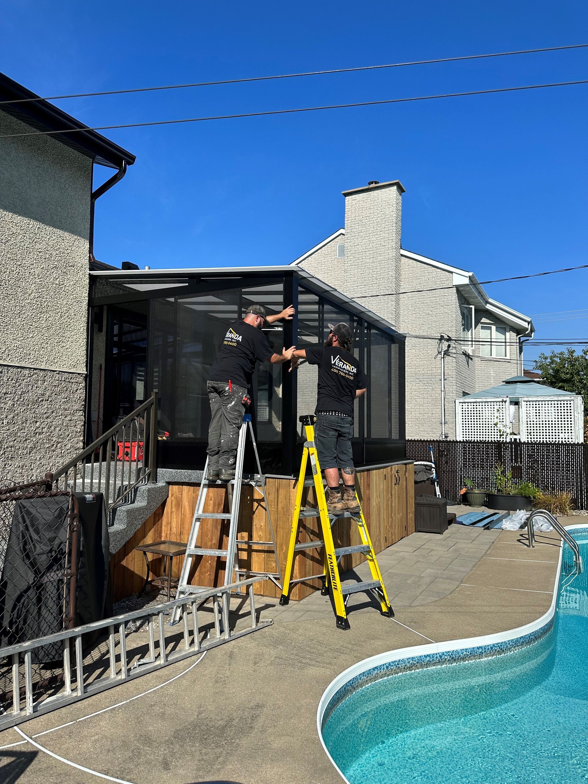 Deux hommes travaillent sur une véranda à côté d'une piscine.