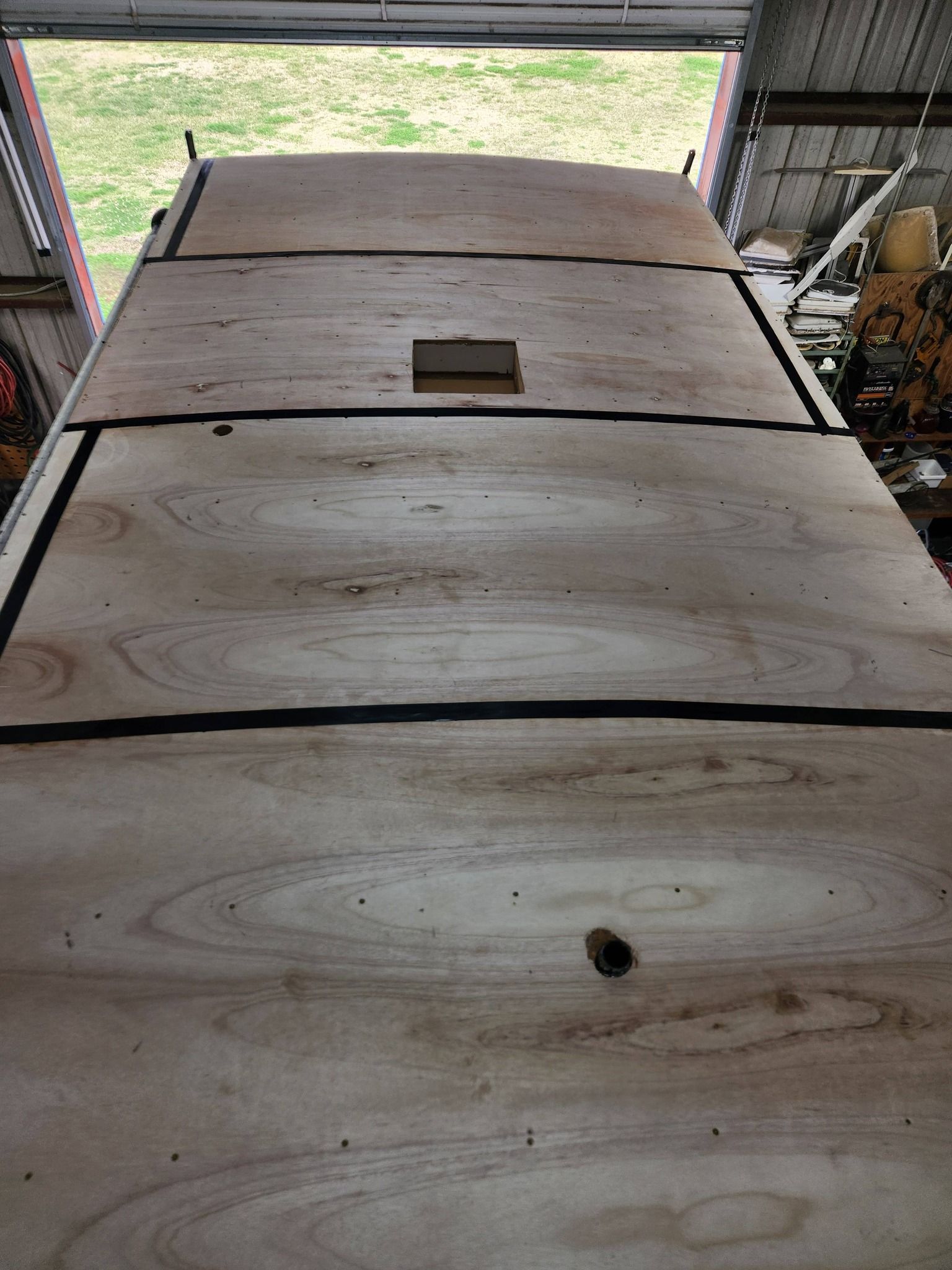 Wooden tabletop with a central slot, viewed from inside a garage toward an open door.