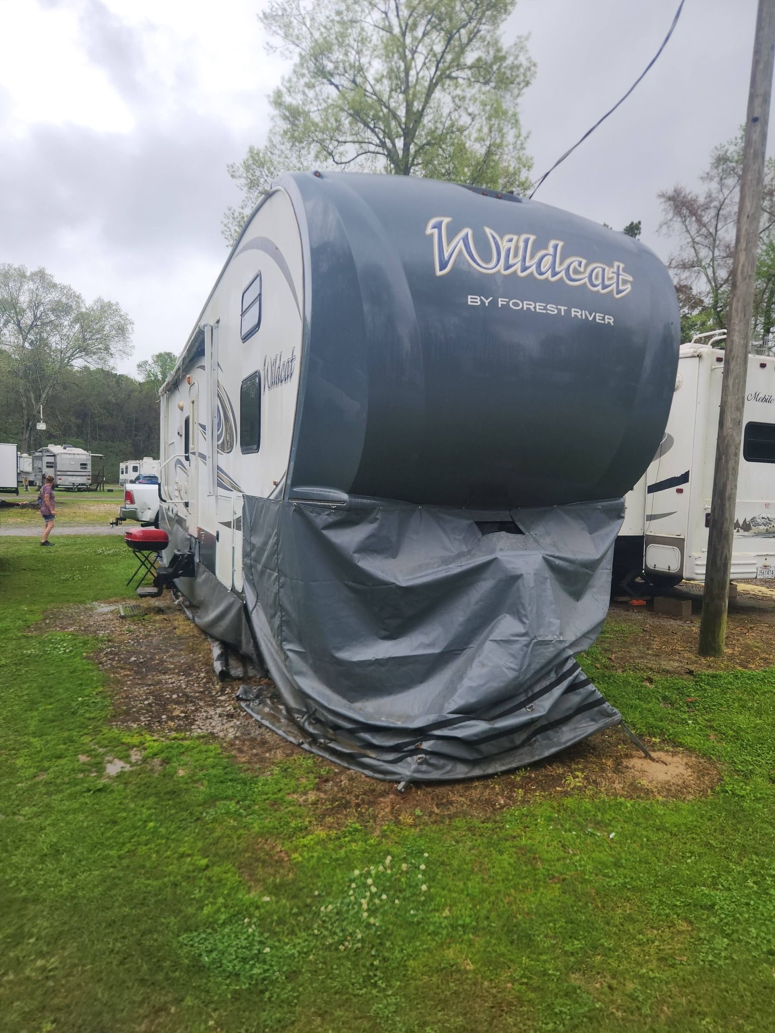 Black-and-gray travel trailer with covered front, parked on grass at an RV site