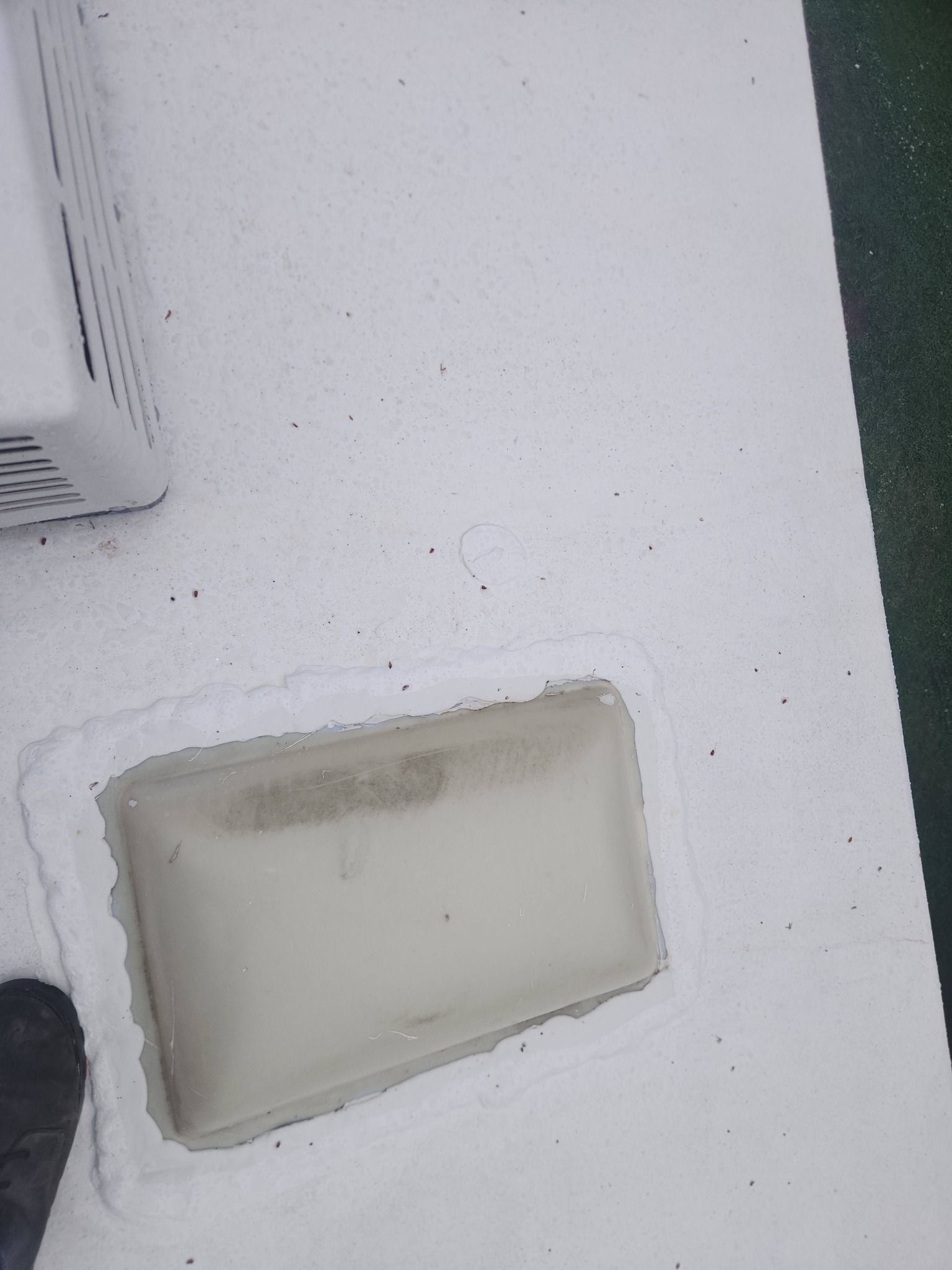 Beige wall vent or access panel on a white textured wall, with a dark object at the left edge.