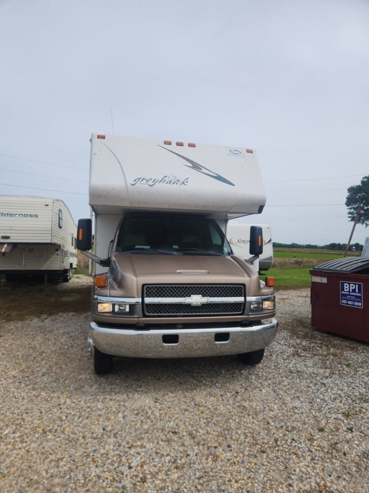 White RV parked on gravel in an open lot under an overcast sky