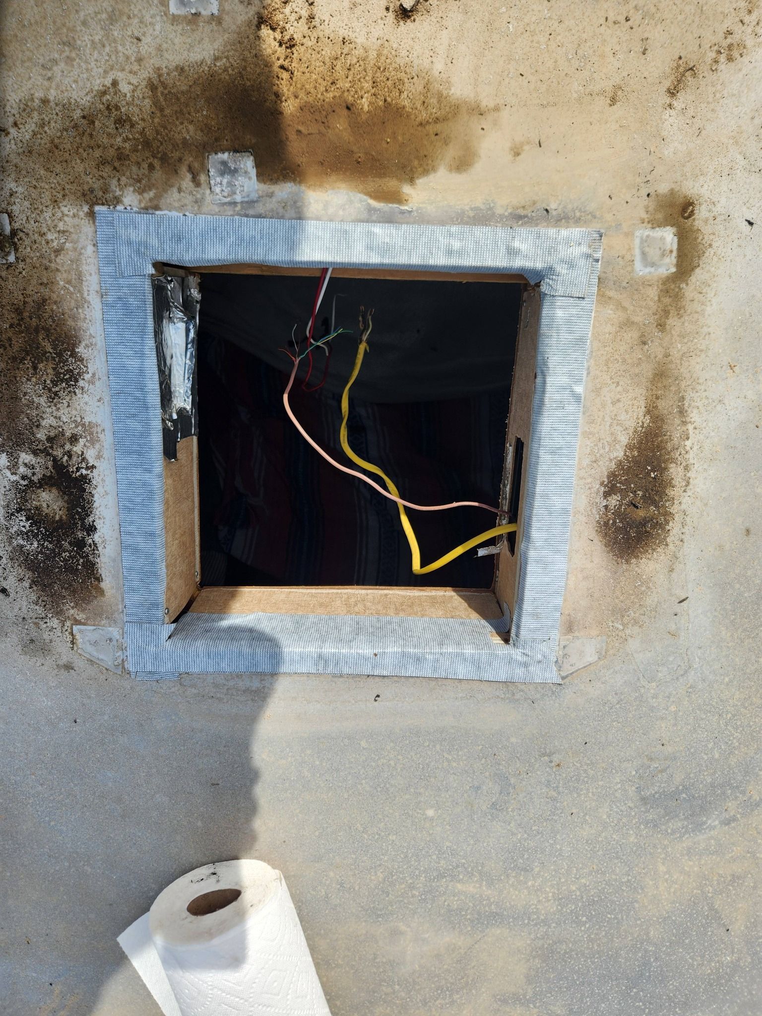 Open wall access panel with exposed wires and a paint roller below, showing a rough repair area