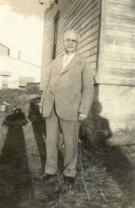 A man in a suit and tie is standing in front of a wooden building.