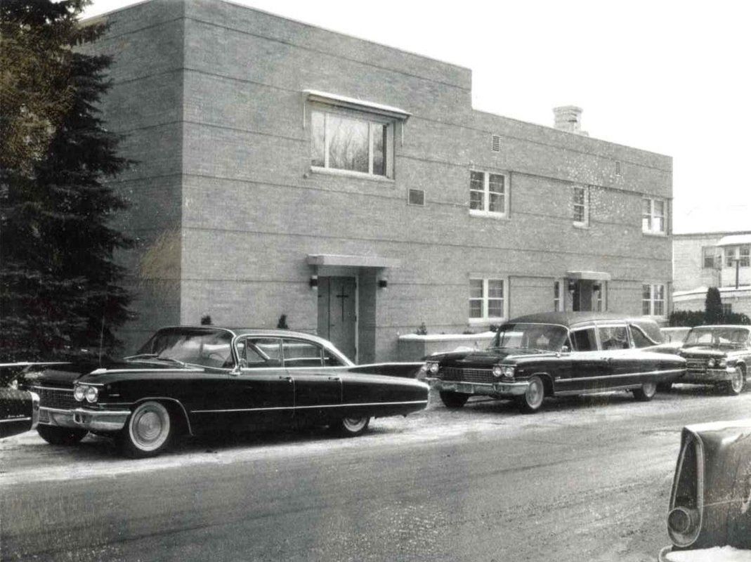 A black and white photo of cars parked in front of a building