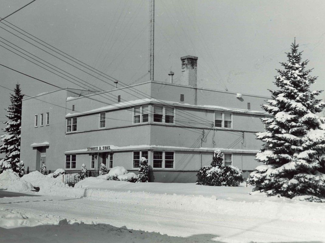 A black and white photo of a row of cars parked in front of a building.