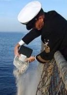 A man in a navy uniform is throwing something into the ocean.