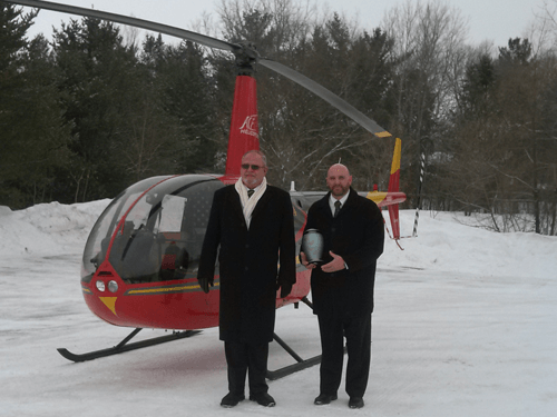 Two men are standing in front of a red helicopter