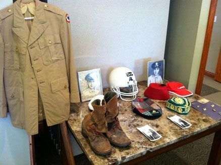 A table with a military uniform , boots , hats and a football helmet on it