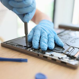 A person wearing blue gloves is working on a laptop