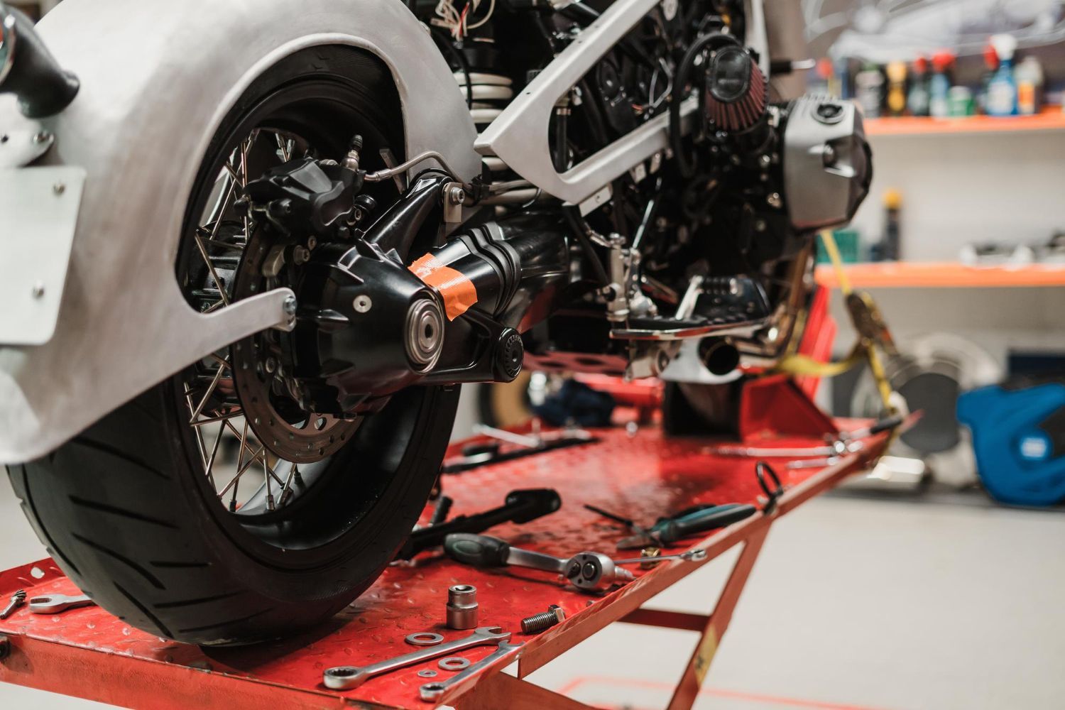 Motorcycle rear wheel and suspension on a red lift, surrounded by tools in a garage setting.