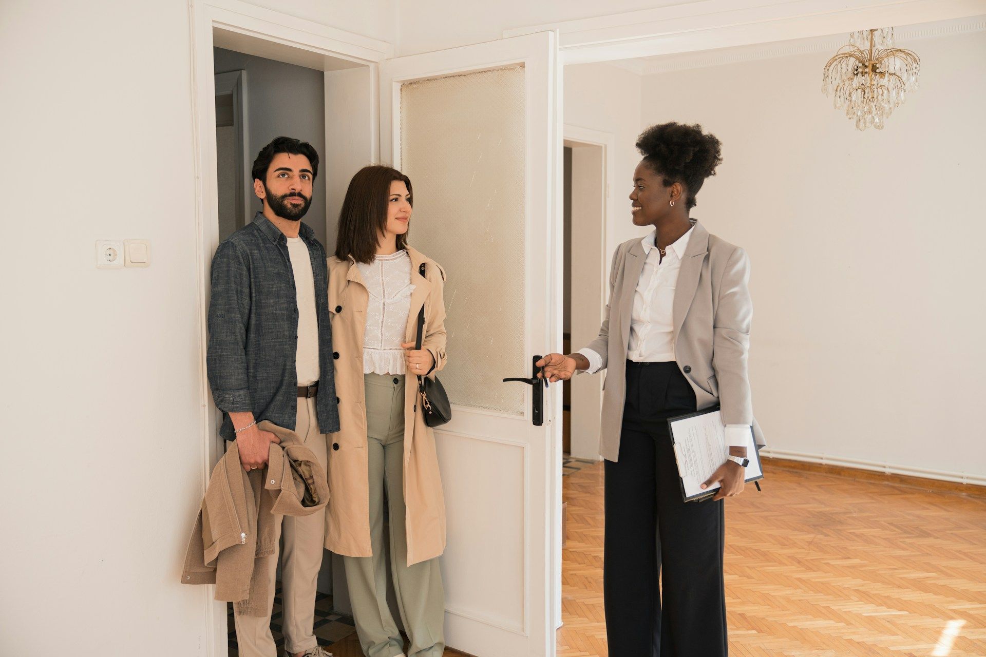 A realtor showing a couple an empty apartment. They are standing near a doorway.