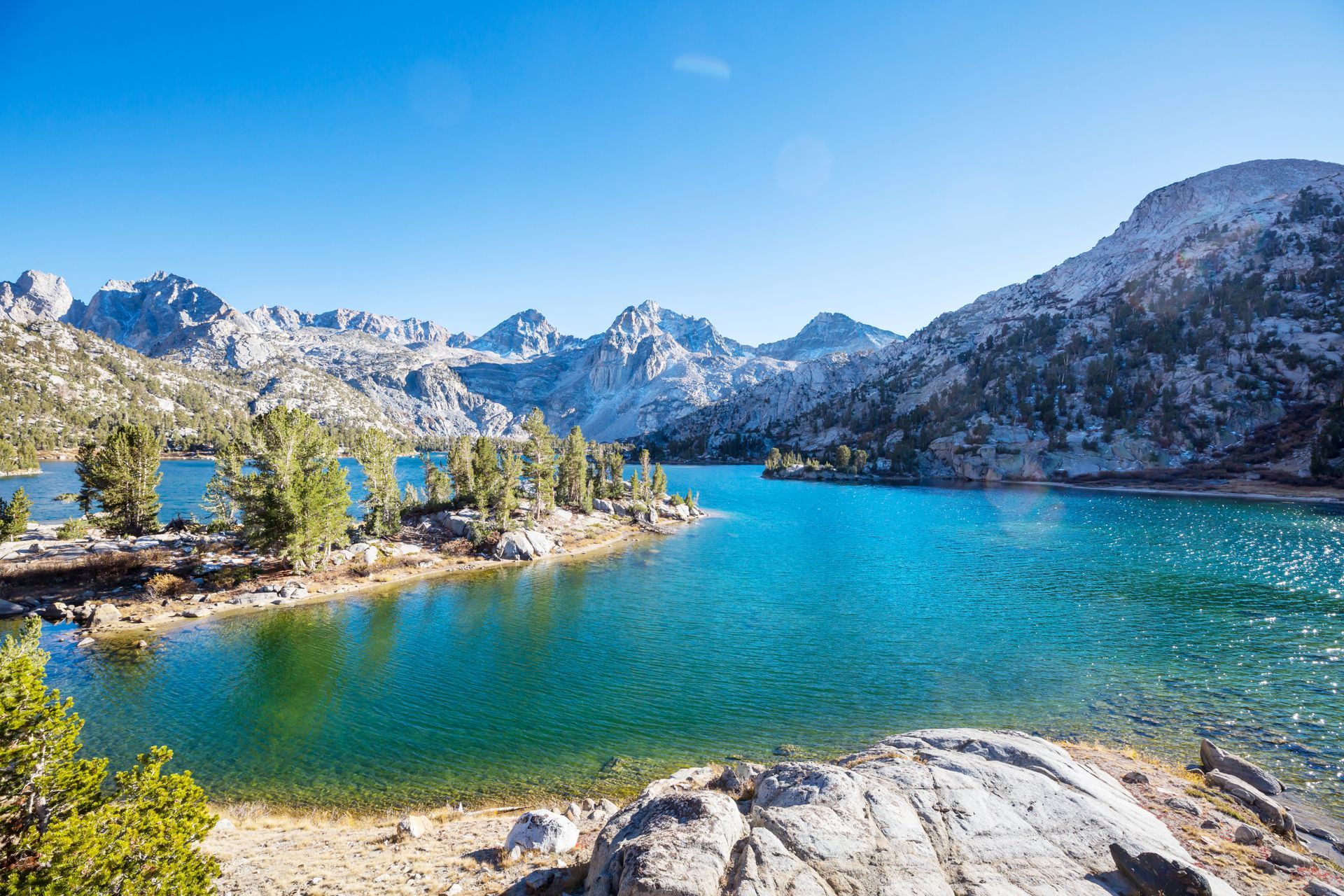 Blue lake surrounded by mountains and trees under a clear blue sky.