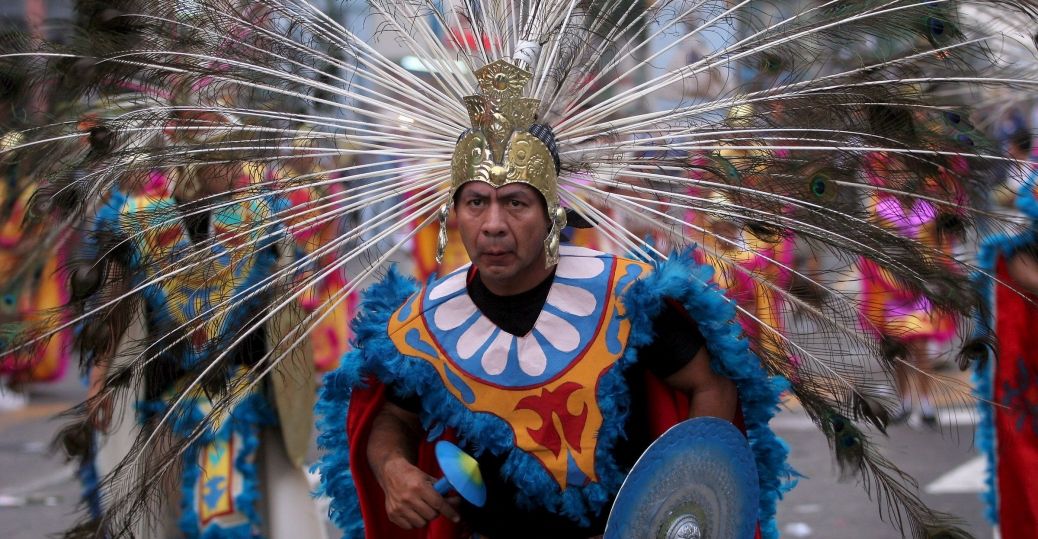 Man in elaborate feathered headdress and costume, possibly a cultural parade or performance.