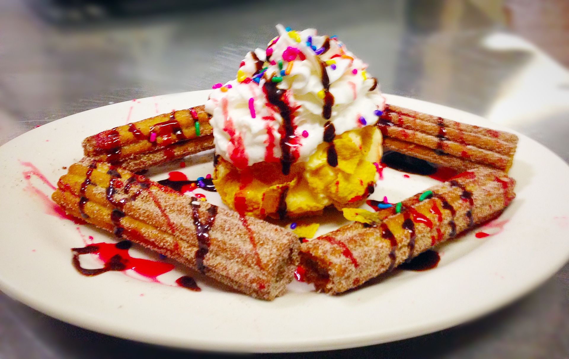Plate of churros, ice cream, whipped cream, sprinkles, and syrup.