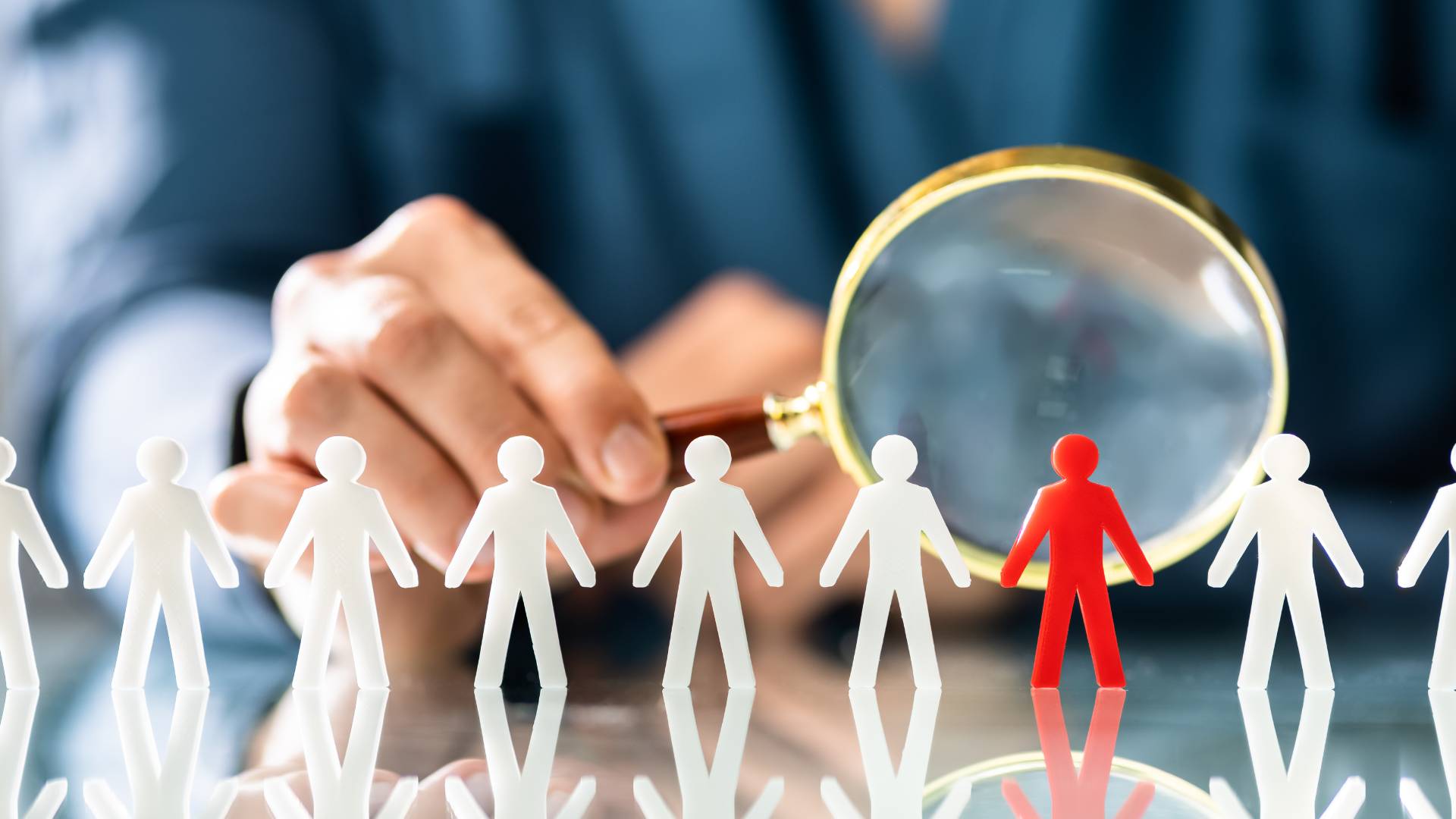 A person is holding a magnifying glass over a group of paper people.