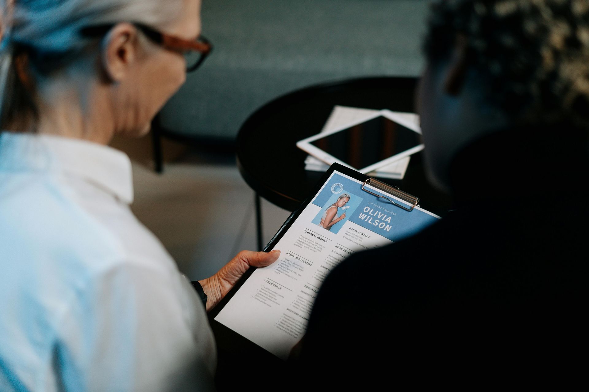 A woman is sitting at a table looking at a resume.