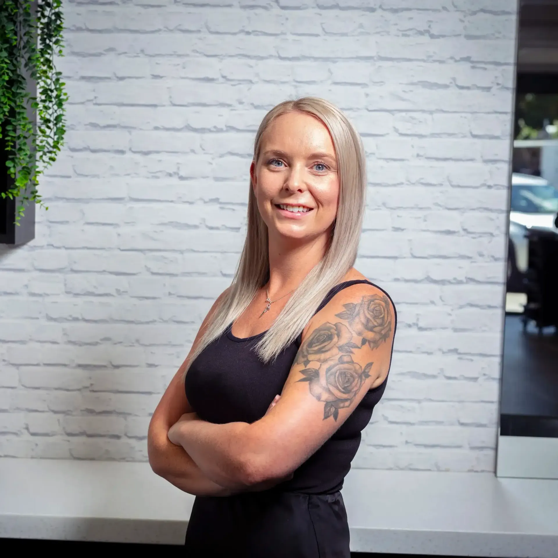 a woman is standing with her arms crossed in front of a white brick wall .