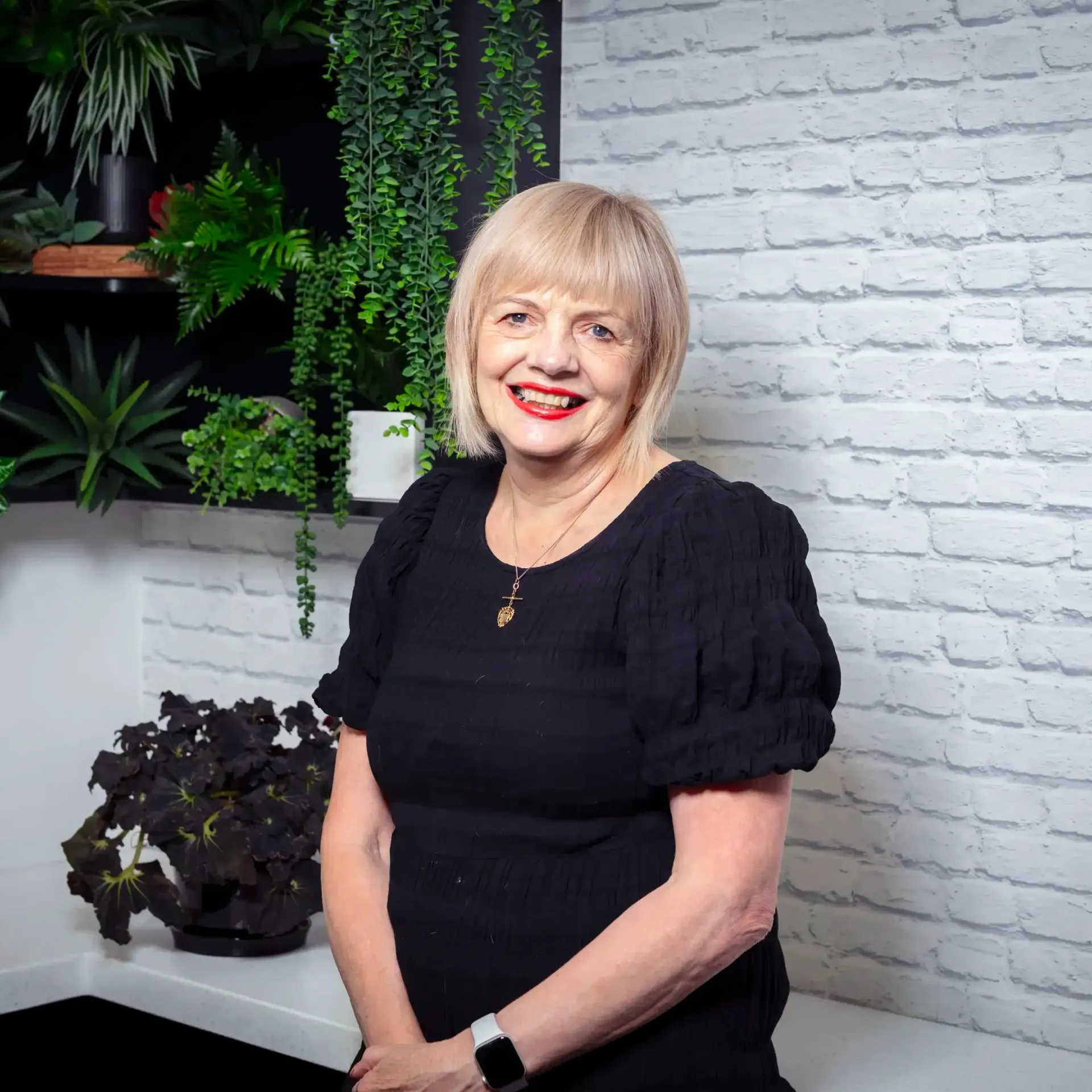 a woman in a black dress is standing in front of a white brick wall .