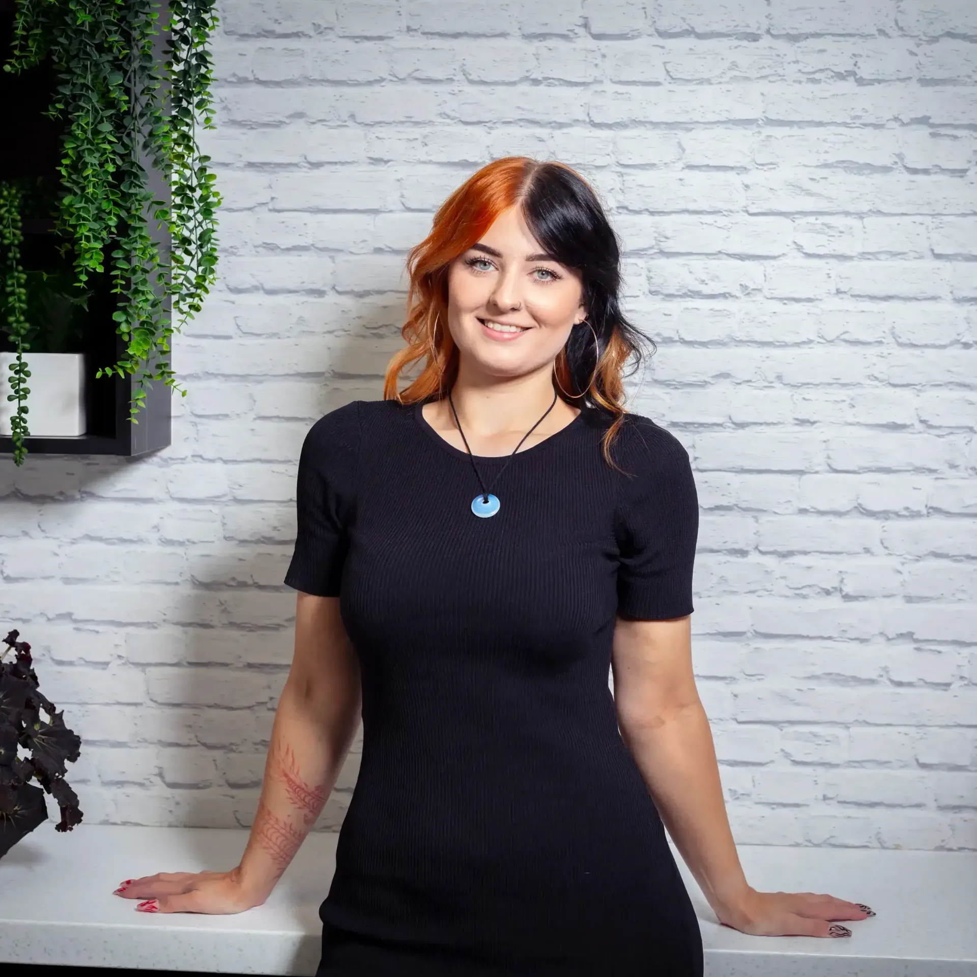 a woman in a black dress is standing in front of a white brick wall .