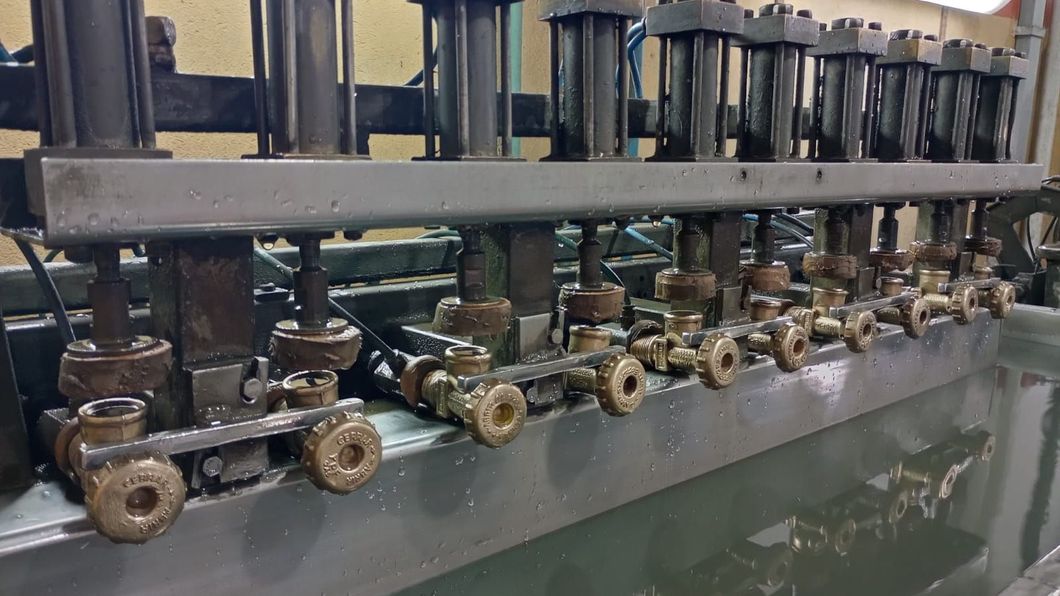 Piezas metálicas en baño líquido, procesadas por maquinaria automatizada. Entorno industrial.