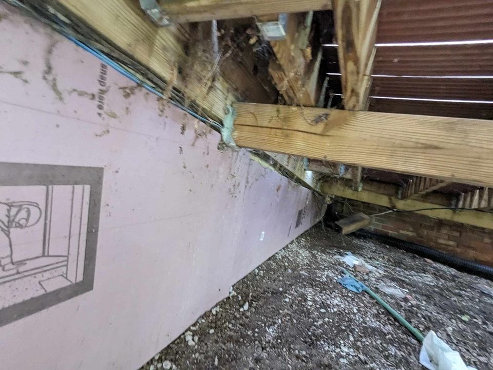 Wooden beams and siding with pink insulation in a crawl space. Debris covers the floor.
