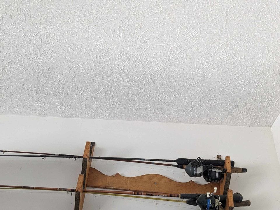 Fishing rods on a wooden rack, mounted on a white wall, under a textured ceiling.
