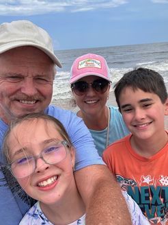 Family selfie on a beach. Smiling adults with two children. Ocean in background, sunny day.