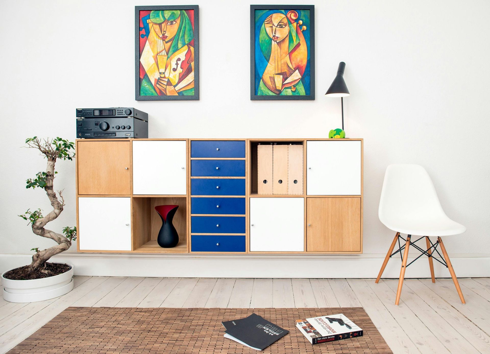 Modern living room with floating storage, bonsai tree, artwork, and a chair.