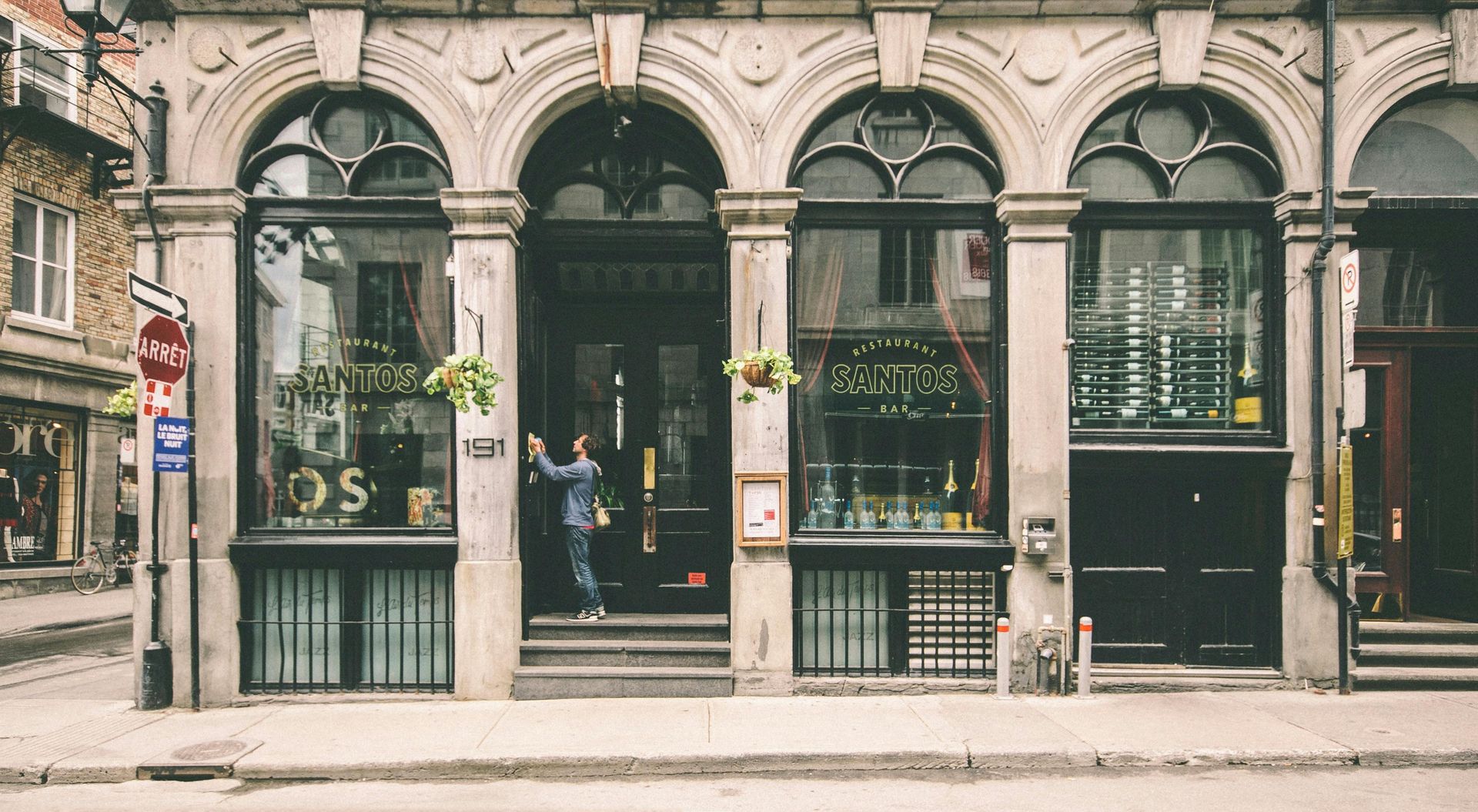 Storefront with arched windows, a person entering, street sign, stone facade.