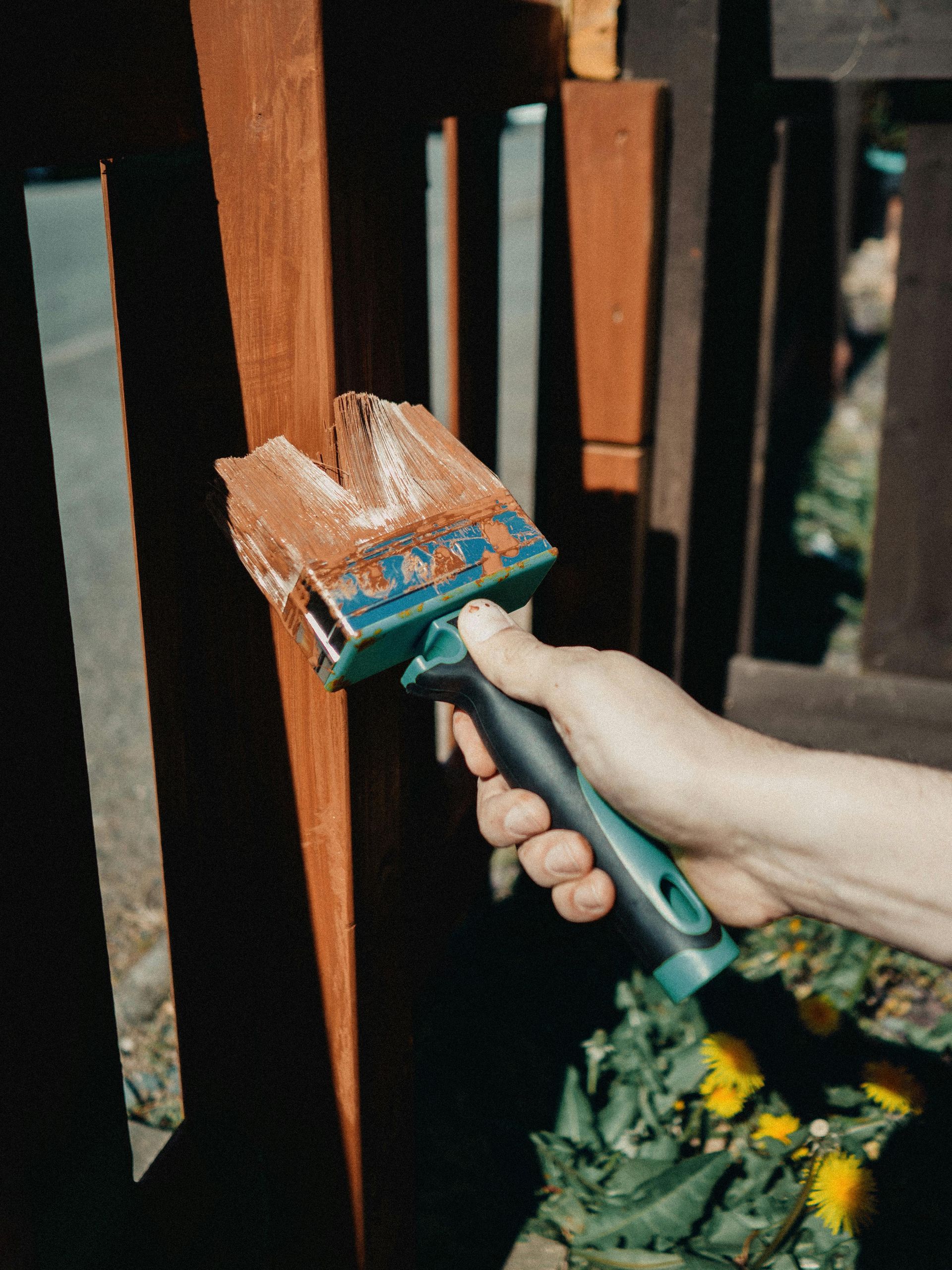 Person's hand with paint brush painting wooden art installation outdoors.