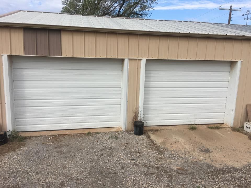 Two white garage doors on a tan building, gravel driveway.