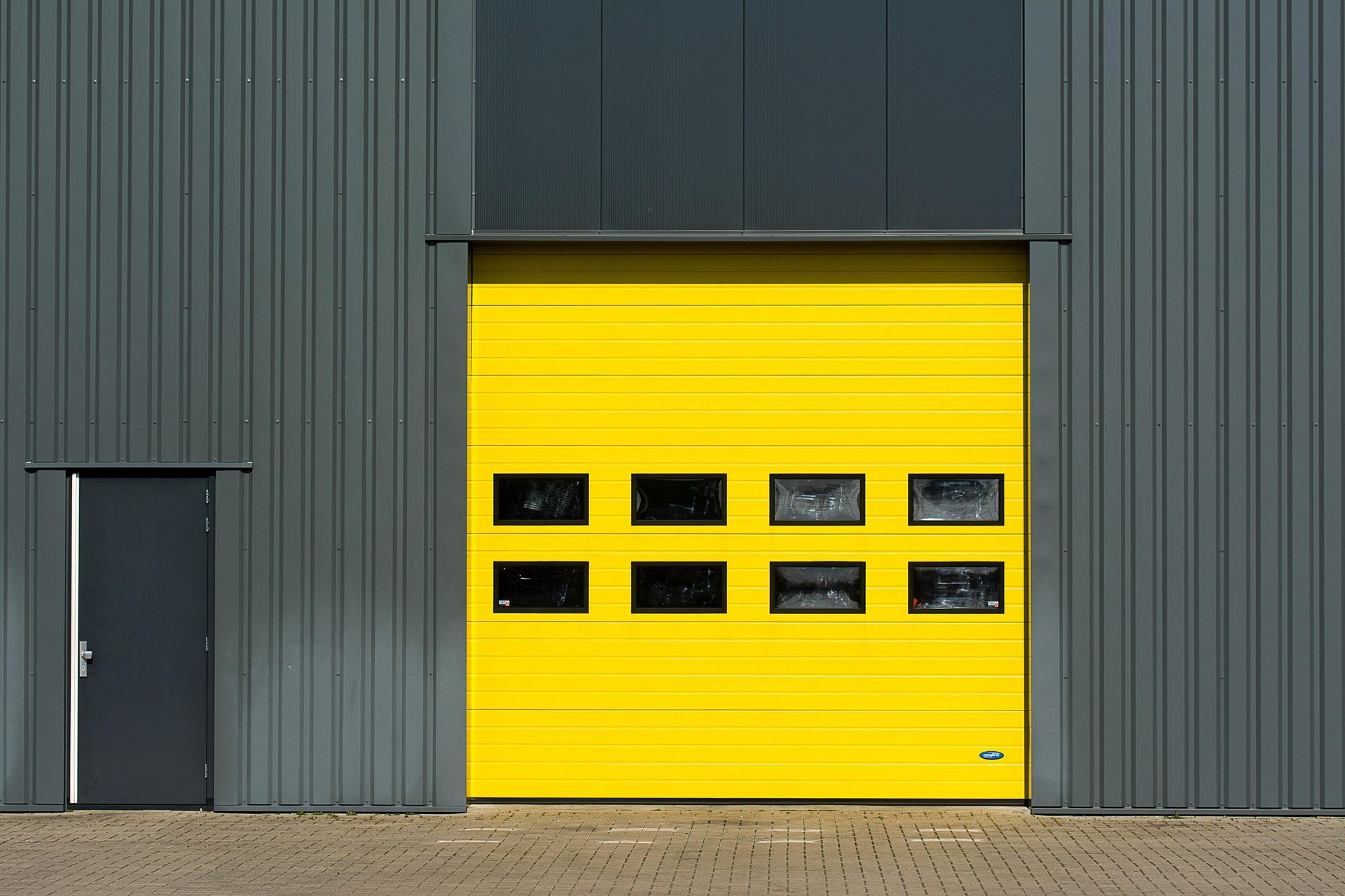 Yellow industrial garage door with windows, gray building, and a side door.
