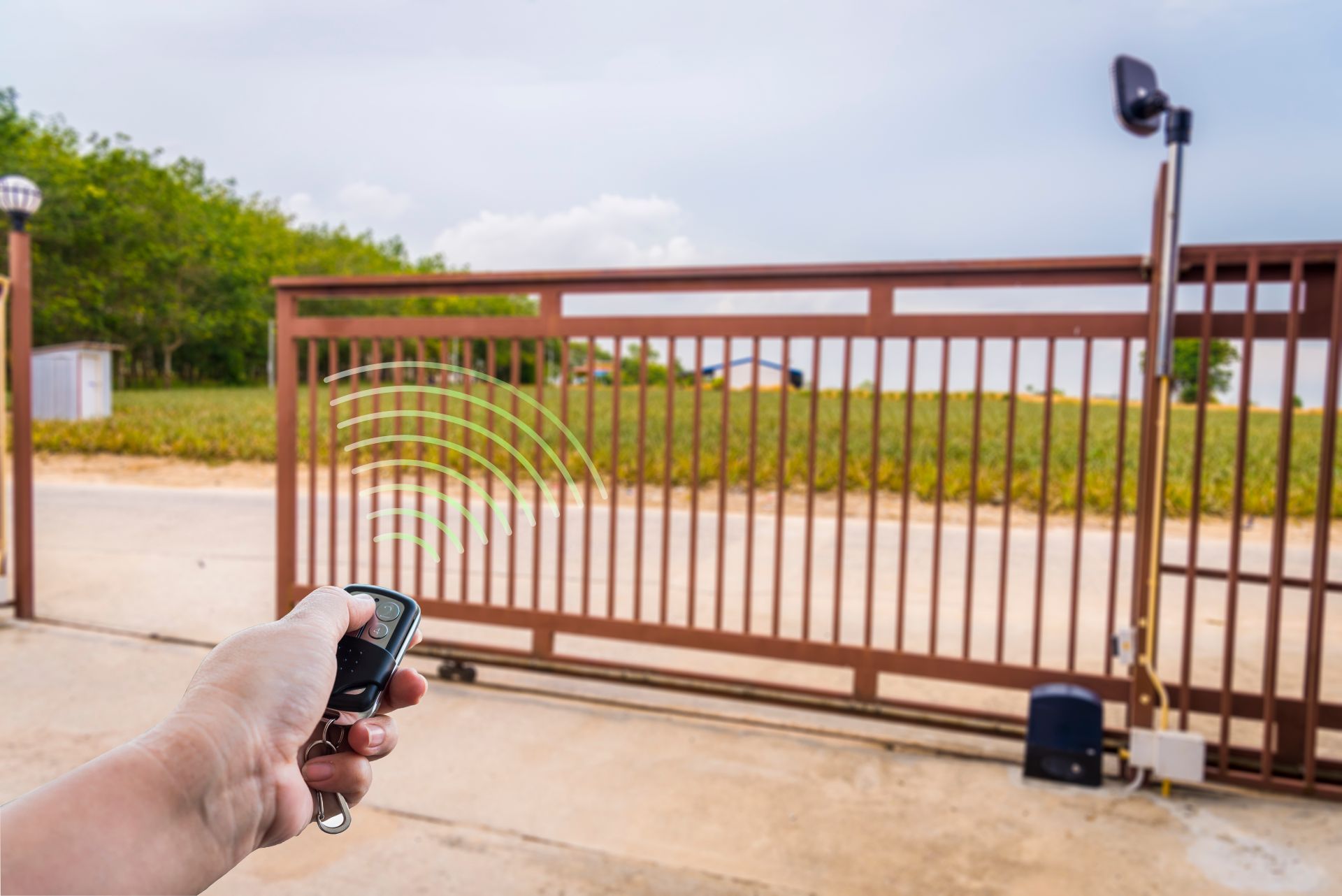 Person using remote to open a brown sliding gate on a concrete driveway, outdoors.