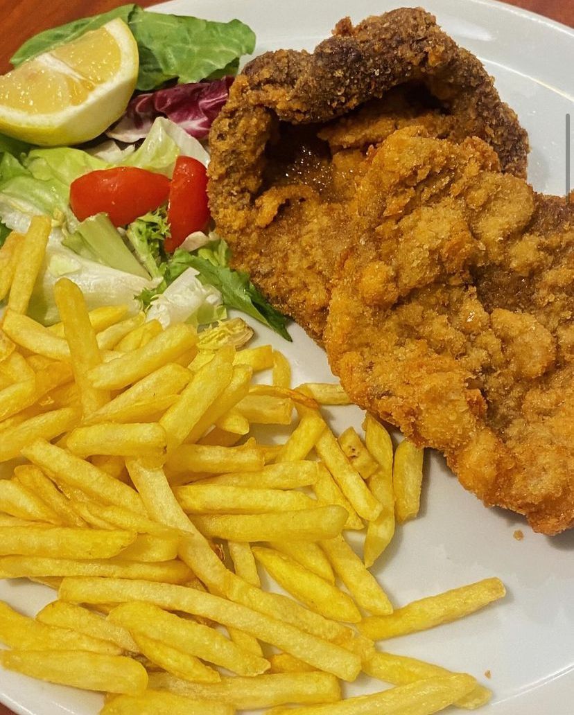 Un piatto bianco con sopra pollo fritto e patatine fritte.