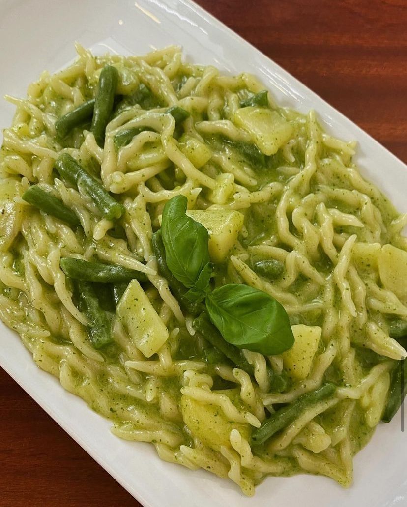 Un piatto bianco con sopra tagliatelle, fagiolini e basilico su un tavolo di legno.