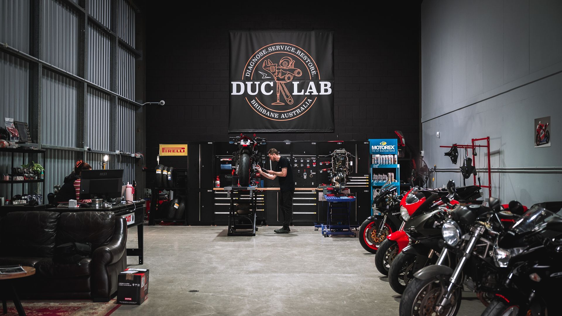 the duc lab workshop, ducati motorcycles lined up and a technician working.