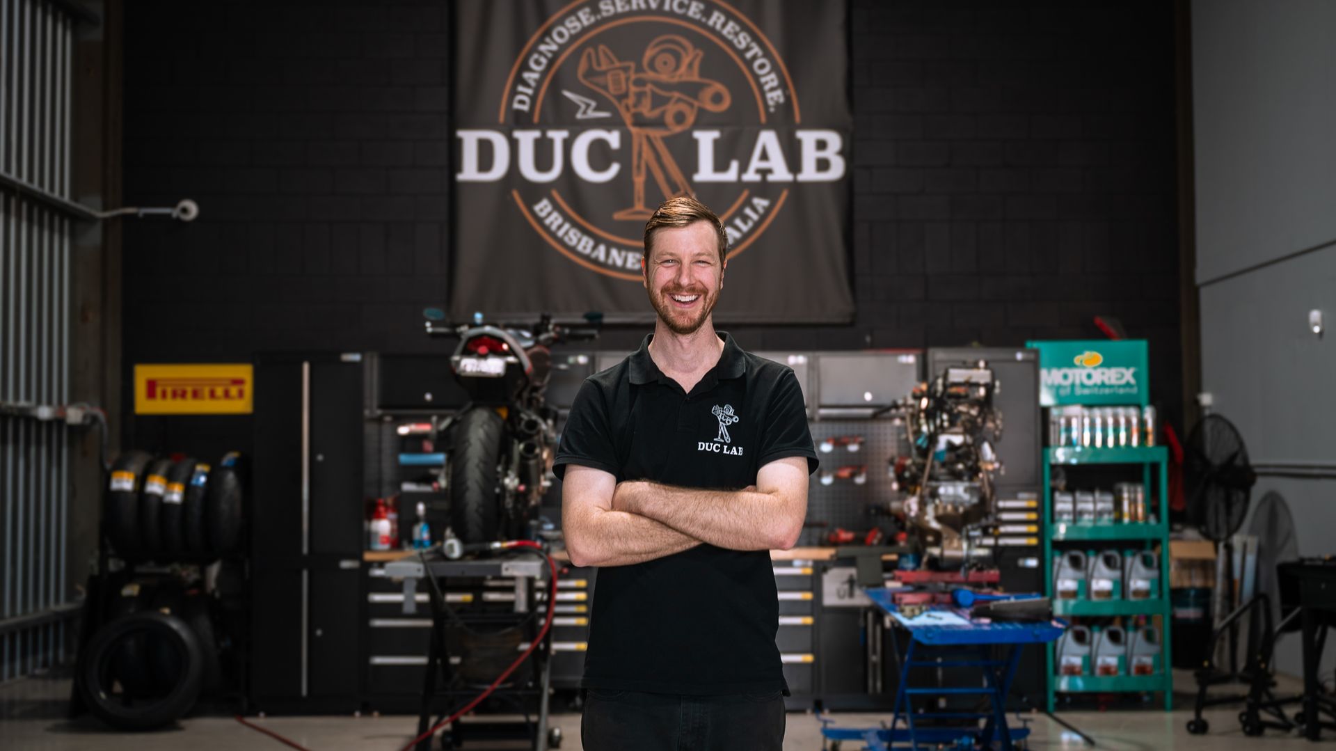 Duc Lab owner Ash proudly standing in front of his ducati motorcycle workshop.
