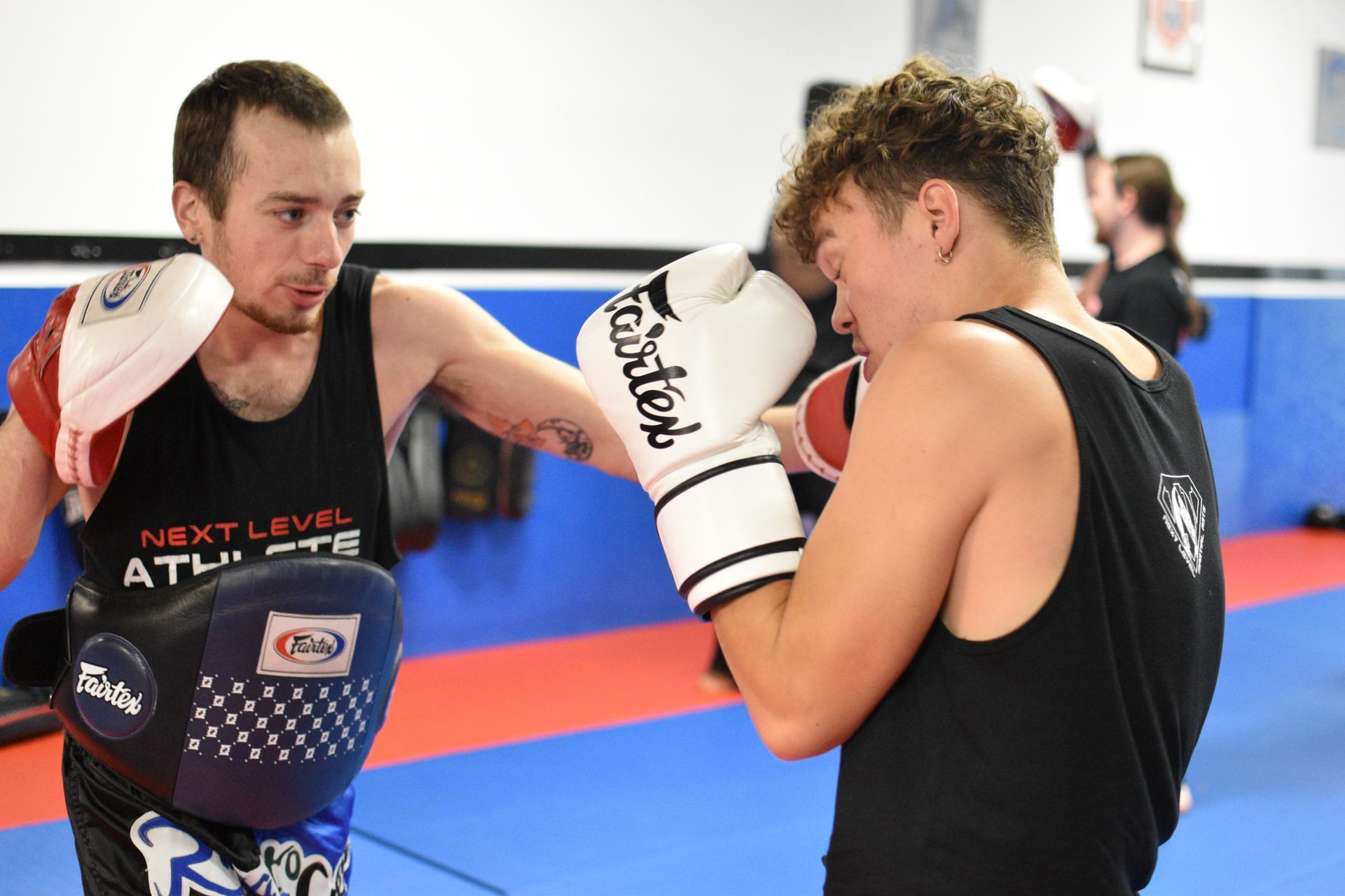 Two men wearing fairtex boxing gloves are sparring in a gym.