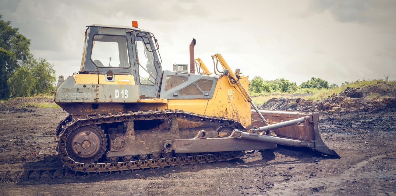 A yellow and gray bulldozer parked on a muddy, dirt-filled work site under a cloudy sky.