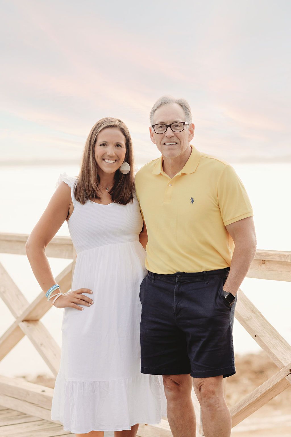Three people on a beach wearing matching coral shirts. Woman in pink shorts, men in khaki shorts.