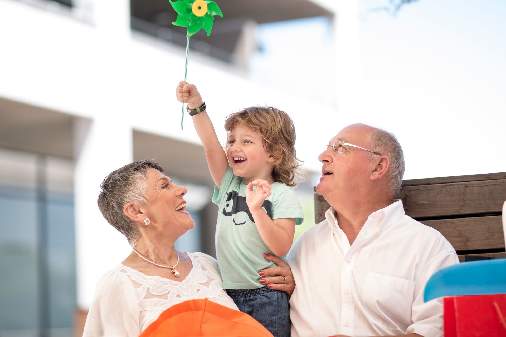 Grandparents with two grandchildren smiling outdoors in a grassy area.