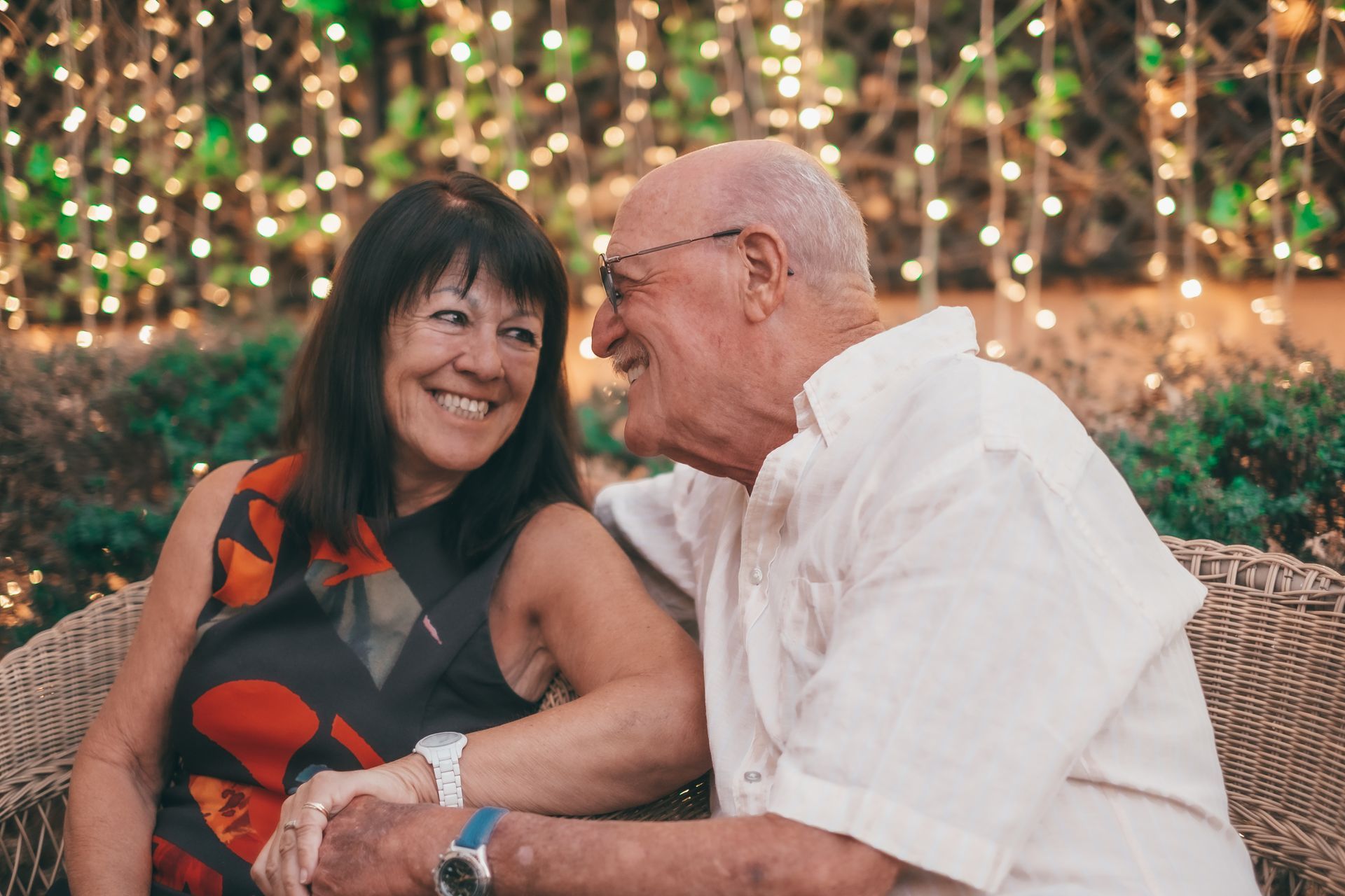 Grandparents with two grandchildren smiling outdoors in a grassy area.