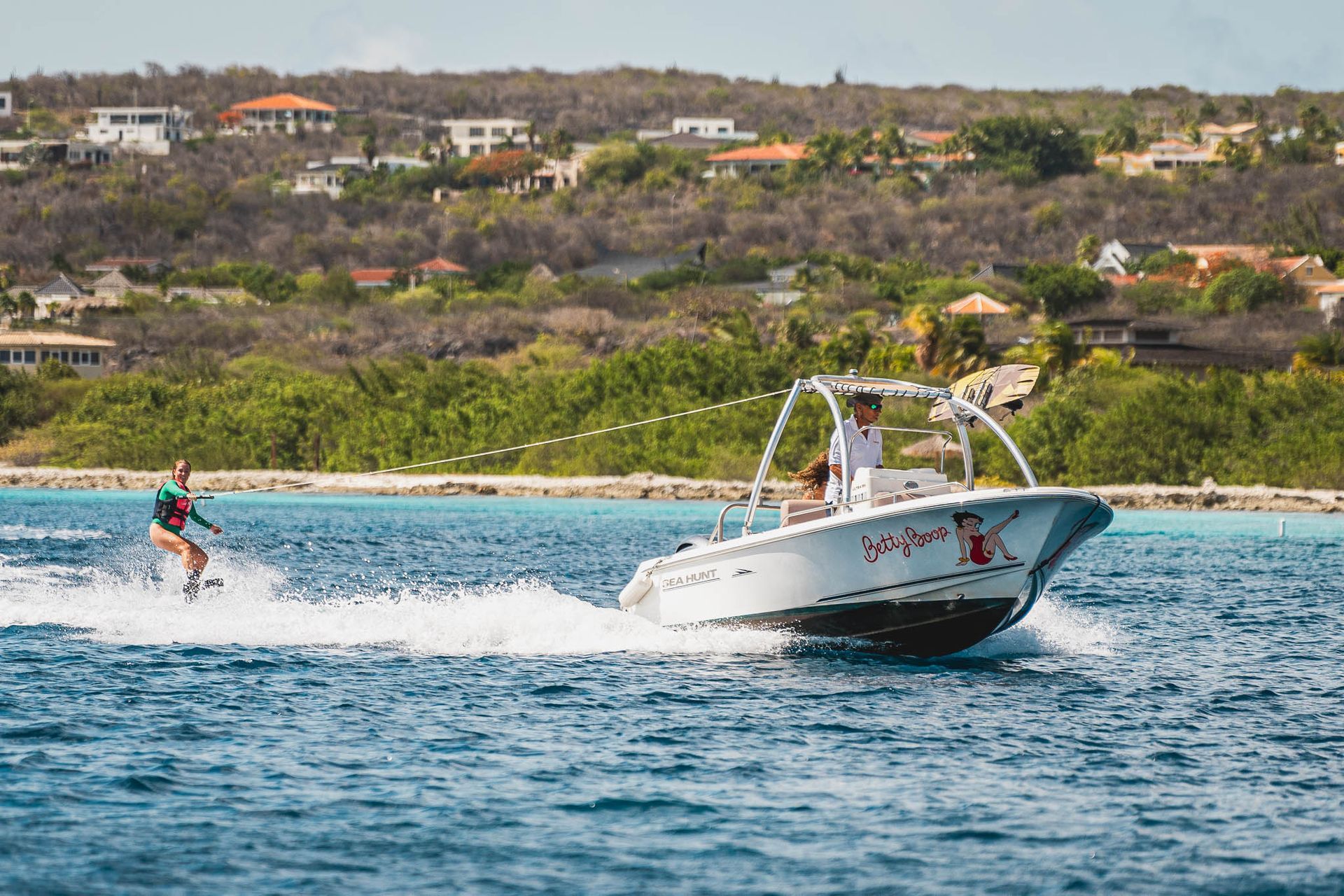 Blue Bay Bonaire Verhuur Motorboot vaart over de Caribische Zee bij Bonaire, jonge vrouw doet aan wakeboarden.