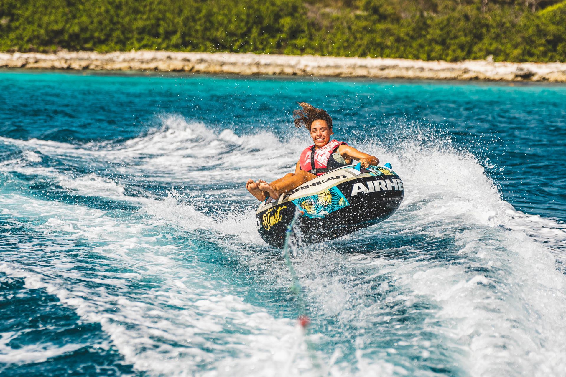 Blue Bay Bonaire Verhuur boot, jonge vrouw zit in een tube die door motorboot wordt gesleept en lacht.